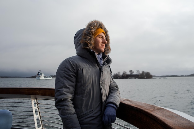 Young caucasian boy in winter jacket stays on boat deck and enjoy sailing in the sea