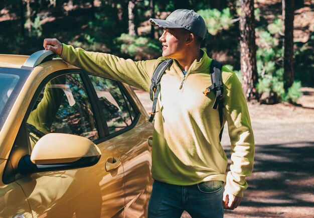 Young Caucasian Boy in Yellow Ready for a Trekking Day Stands Smiling Close to his Yellow Car