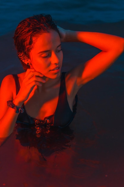 A young Caucasian brunette bathing at night in the sea with an illuminated red light