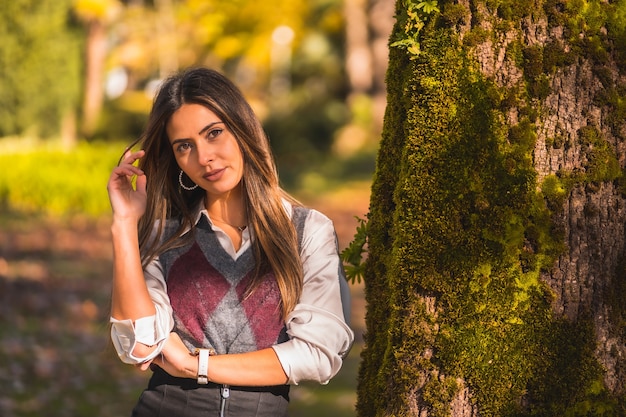 A young Caucasian brunette, in a park next to a tree one autumn afternoon