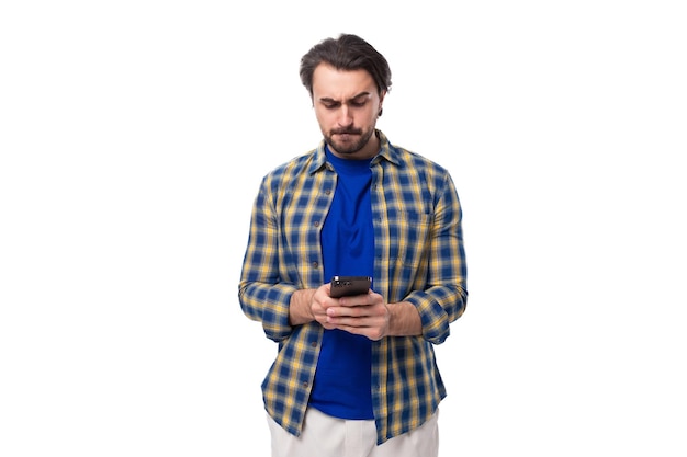 Young caucasian brunette with a beard is dressed in a blue plaid shirt and tshirt watching a video