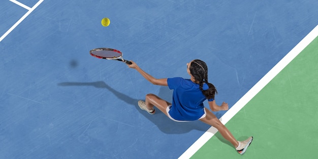 Young caucasian brunette woman in blue shirt playing tennis at the court. Hits ball with racket, outdoors. Youth, flexibility, power, energy. Copyspace. Top view. Motion, action, healthy lifestyle.