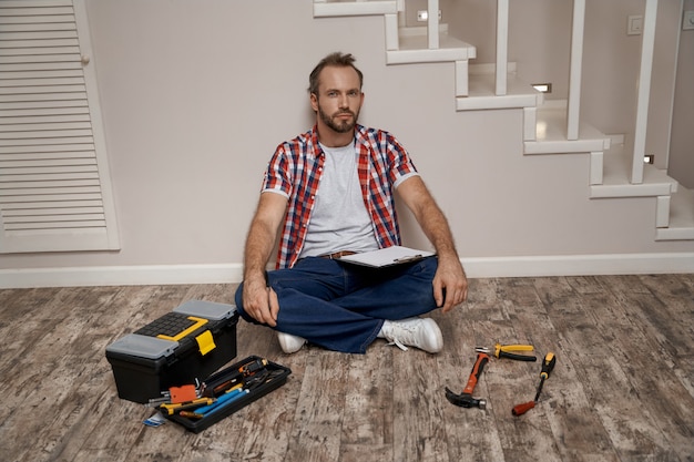 Young caucasian builder sitting on floor near repair tools