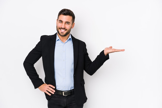 Young caucasian business man against a white wall isolated showing a copy space on a palm and holding another hand on waist.