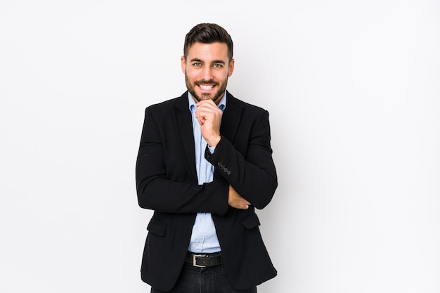 Young caucasian business man against a white wall isolated smiling happy and confident, touching chin with hand.