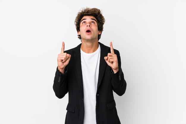Young caucasian business man against a white wall pointing upside with open mouth.