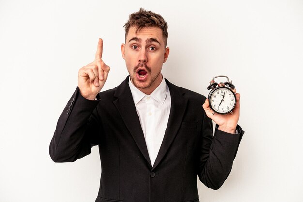 Young caucasian business man holding alarm clock isolated on white background having an idea, inspiration concept.