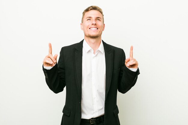 Young caucasian business man indicates with both fore fingers up showing a blank space.