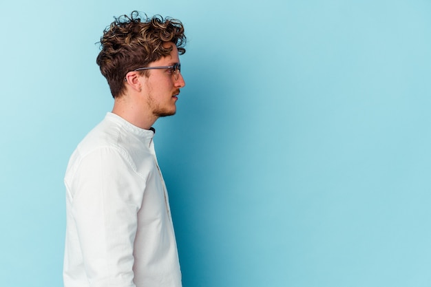 Young caucasian business man isolated on blue wall gazing left, sideways pose.