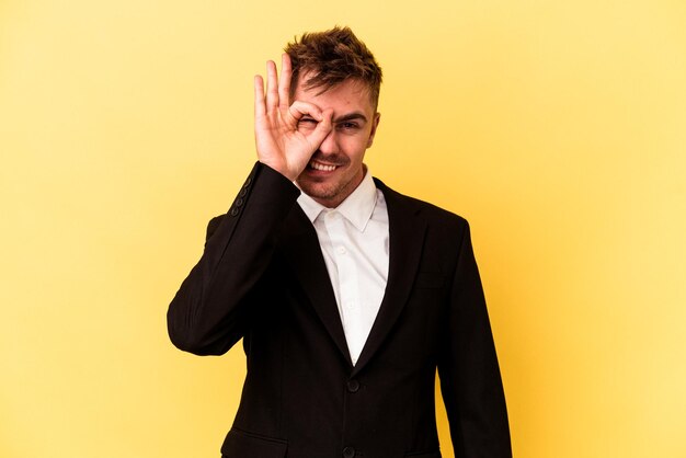 Young caucasian business man isolated on yellow background excited keeping ok gesture on eye.