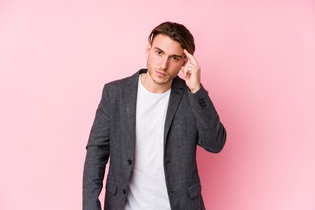 Young caucasian business man posing isolated pointing temple with finger, thinking, focused on a task.