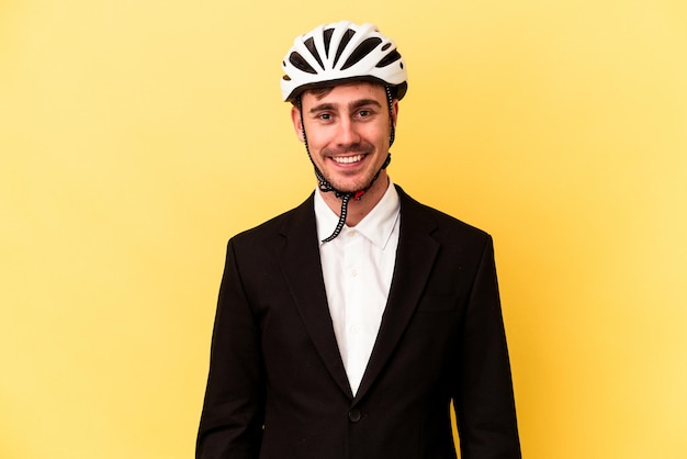 노란색 배경에 격리된 자전거 헬멧을 쓴 젊은 백인 사업가는 행복하고 웃고 쾌활합니다.