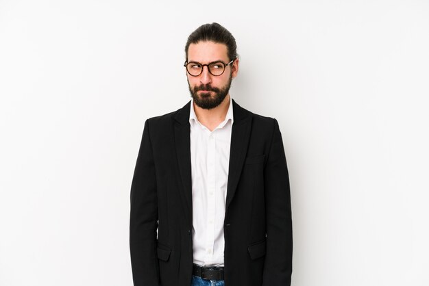 Young caucasian business man on a white wall, feels doubtful and unsure.