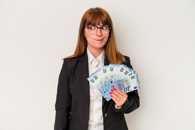 Young caucasian business woman holding bills isolated on white background confused, feels doubtful and unsure.