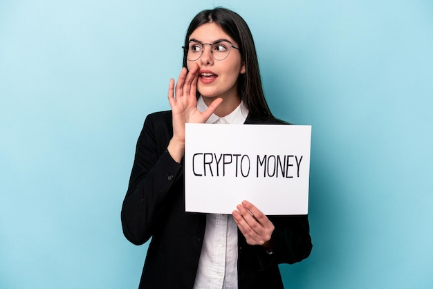 Young caucasian business woman holding a crypto money placard isolated on blue background shouting and holding palm near opened mouth