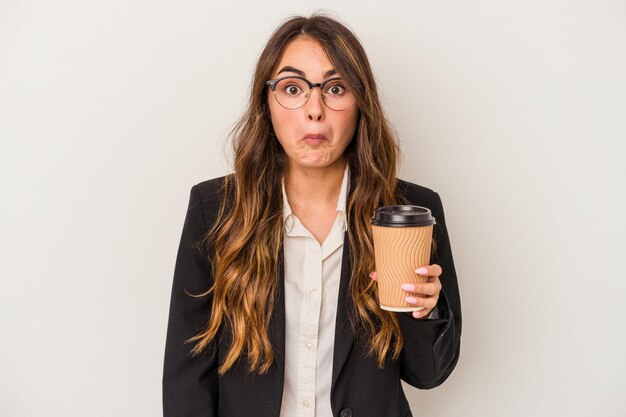 Young caucasian business woman holding a takeaway coffee isolated on white background shrugs shoulders and open eyes confused.