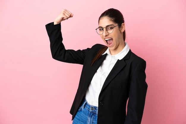 Young caucasian business woman isolated on pink background doing strong gesture