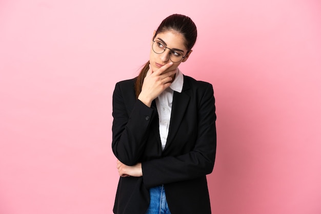 Young caucasian business woman isolated on pink background having doubts and with confuse face expression