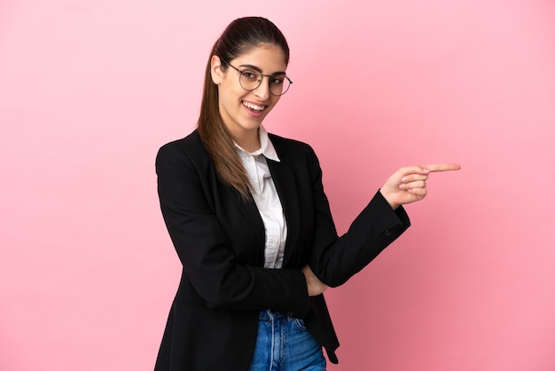 Young caucasian business woman isolated on pink background pointing finger to the side