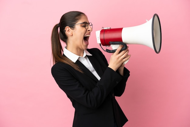 Young caucasian business woman isolated on pink background shouting through a megaphone