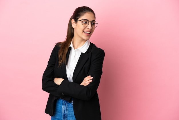 Young caucasian business woman isolated on pink background with arms crossed and happy