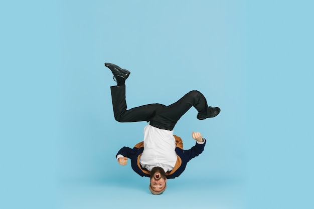 Photo young caucasian businessman having fun dancing break dance on blue studio background