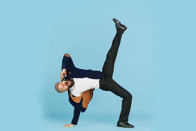 Young caucasian businessman having fun dancing break dance on blue studio background