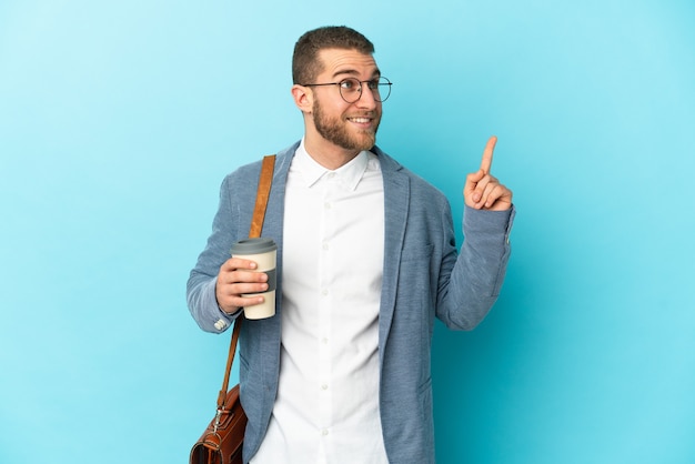 Young caucasian businessman isolated on blue wall pointing up a great idea