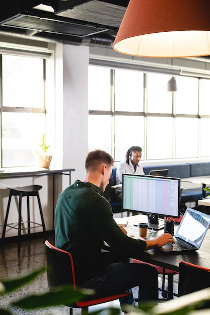 Photo young caucasian businessman using computer and laptop at desk in creative office