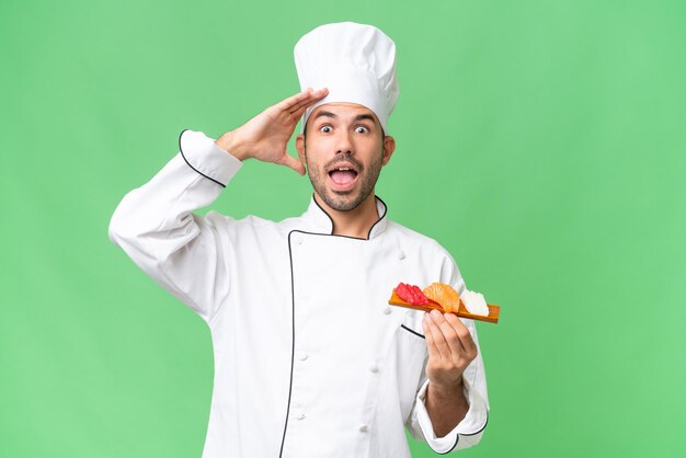 Young caucasian chef holding a sushi over isolated background with surprise expression