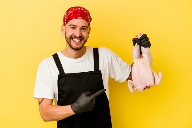 Young caucasian chef man holding chicken isolated on yellow background