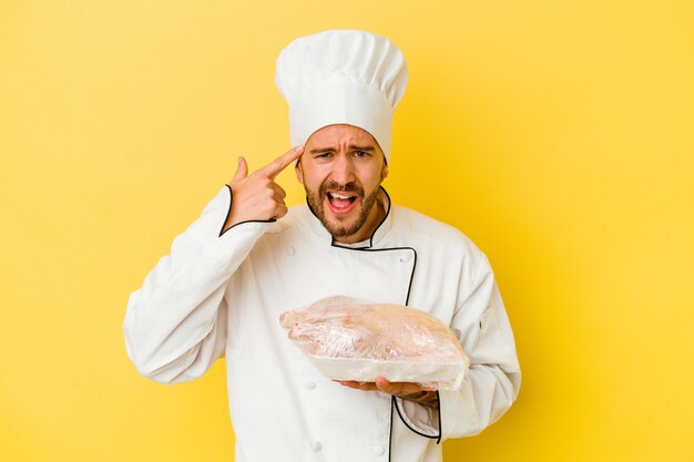 Young caucasian chef man holding chicken isolated on yellow wall showing a disappointment gesture with forefinger.