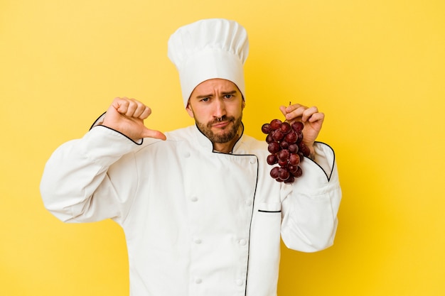 Young caucasian chef man holding grapes isolated on yellow background feels proud and self confident, example to follow.