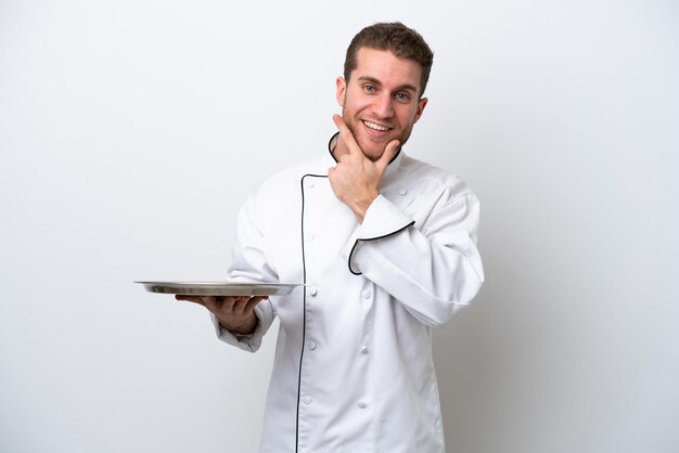 Young caucasian chef with tray isolated on white background happy and smiling