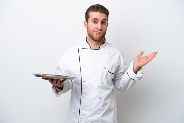 Молодой кавказский шеф-повар с подносом на белом фоне сомневается, поднимая руки