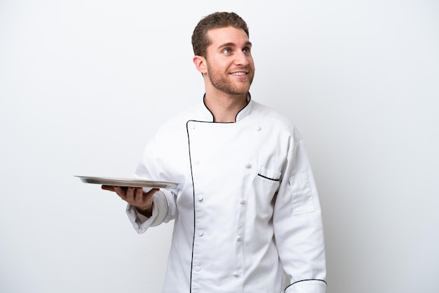 Young caucasian chef with tray isolated on white background thinking an idea while looking up