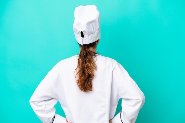 Young caucasian chef woman isolated on blue background in back\
position