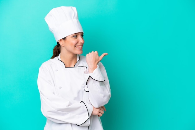 제품을 제시하기 위해 측면을 가리키는 파란색 배경에 고립 된 젊은 백인 요리사 여자