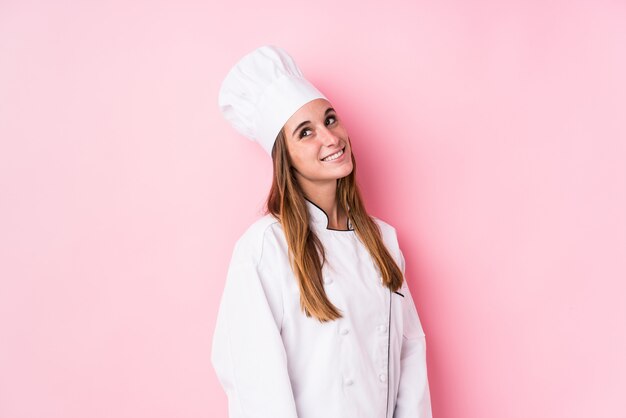 Young caucasian chef woman isolated looks aside smiling, cheerful and pleasant.