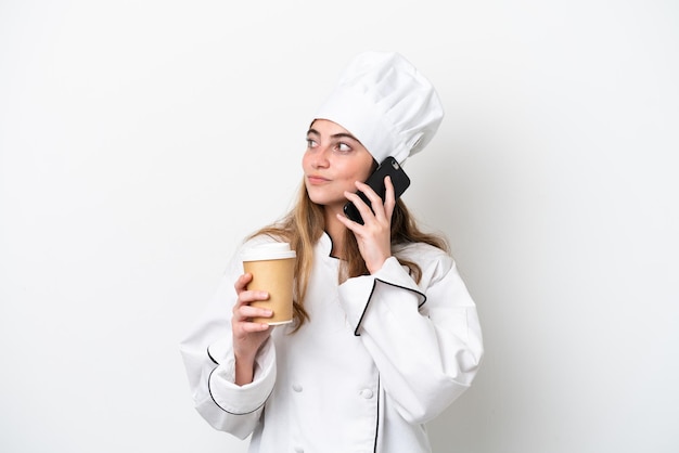 Young caucasian chef woman isolated on white background holding coffee to take away and a mobile