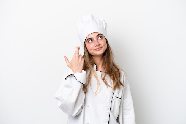 Young caucasian chef woman isolated on white background with fingers crossing and wishing the best