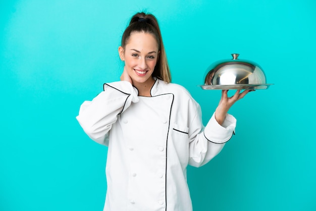 Young caucasian chef woman with tray isolated on blue background laughing