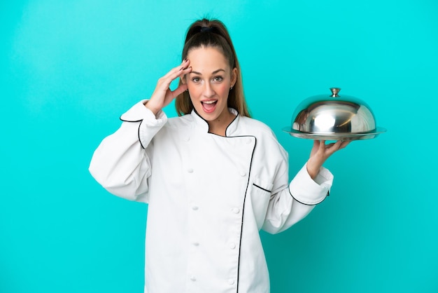 Young caucasian chef woman with tray isolated on blue background with surprise expression