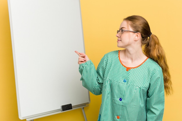 Young caucasian child education teacher explaining on the blackboard isolated on yellow background