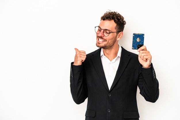 Young caucasian computerized holding HDD isolated on white background points with thumb finger away, laughing and carefree.