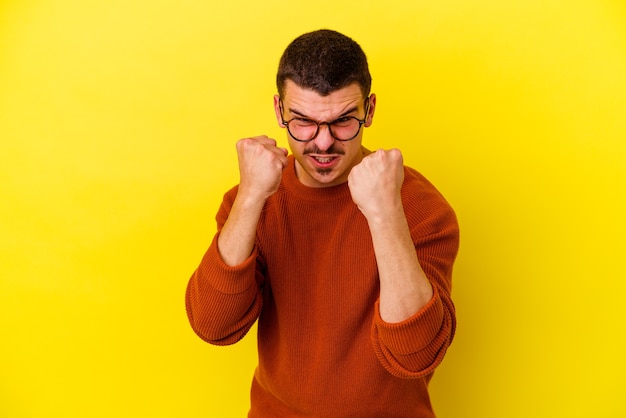 Young caucasian cool man isolated on yellow background showing fist to camera, aggressive facial expression.