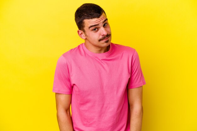 Young caucasian cool man isolated on yellow background shrugs shoulders and open eyes confused.