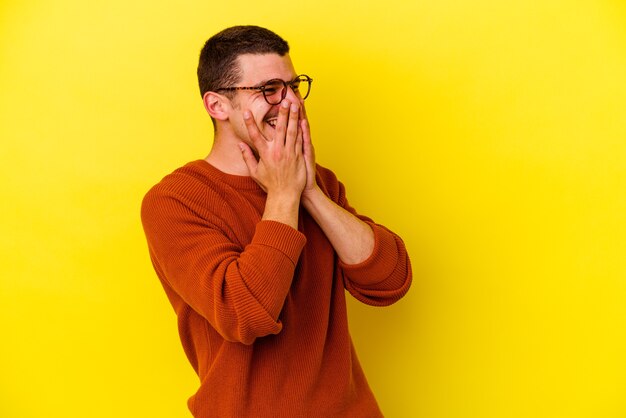 Young caucasian cool man isolated on yellow wall laughing about something, covering mouth with hands.