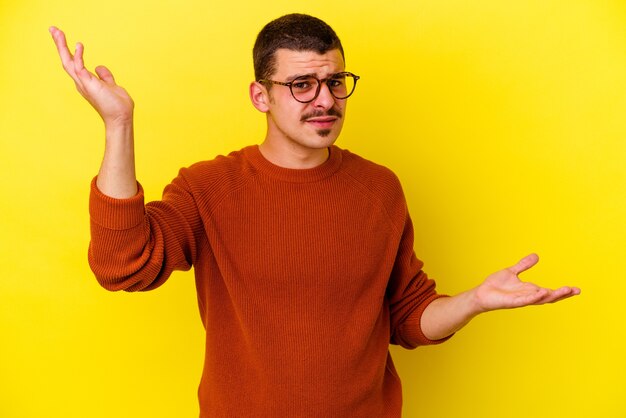 Young caucasian cool man on yellow confused and doubtful shrugging shoulders to hold a copy space.