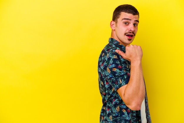 Young caucasian cool man on yellow points with thumb finger away, laughing and carefree.